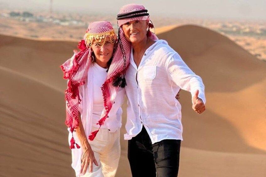 Two people in traditional attire walking on a sand dune. 3