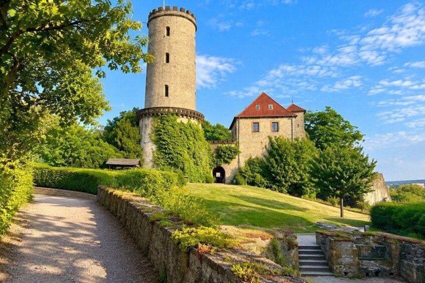 A castle with a tower, a red-roofed building, and a pathway leading to the entrance. 5