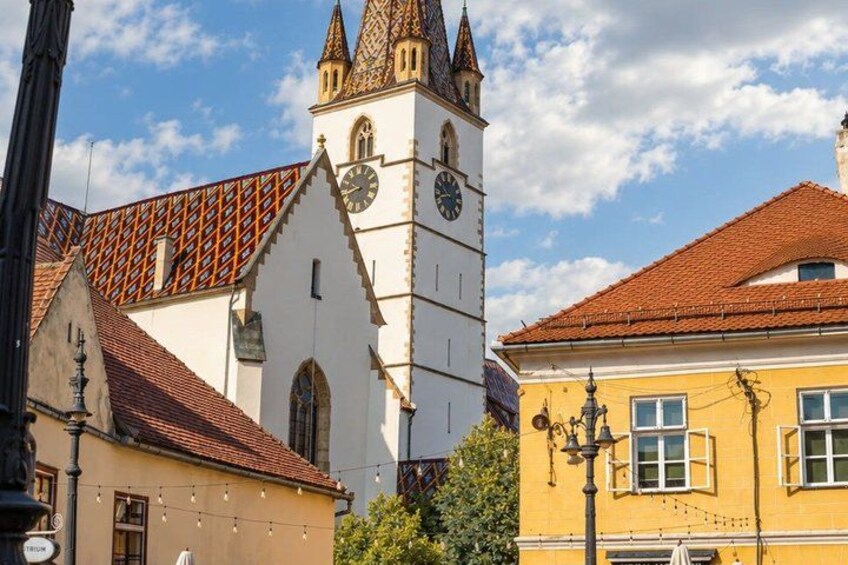 A church with a clock tower, a building with a red roof, and a street lamp. 2
