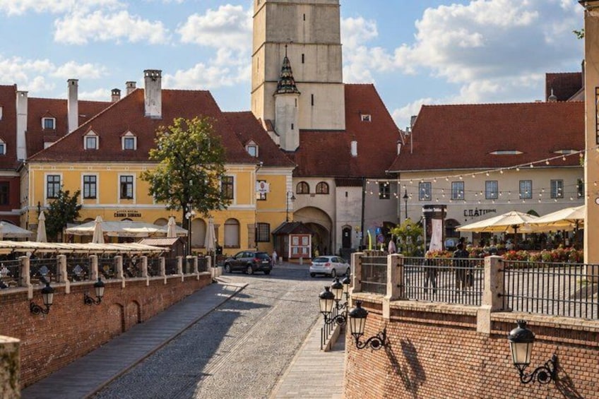 A cobblestone street with buildings, a tower, and outdoor seating areas. 5