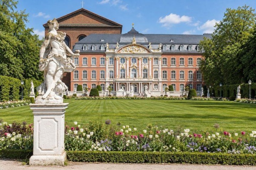 A grand building with a symmetrical facade, manicured garden, and a statue in the foreground. 4