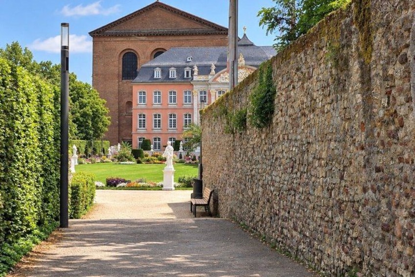 A pathway leading to a large red brick building with a dome, surrounded by a stone wall and greenery. 2