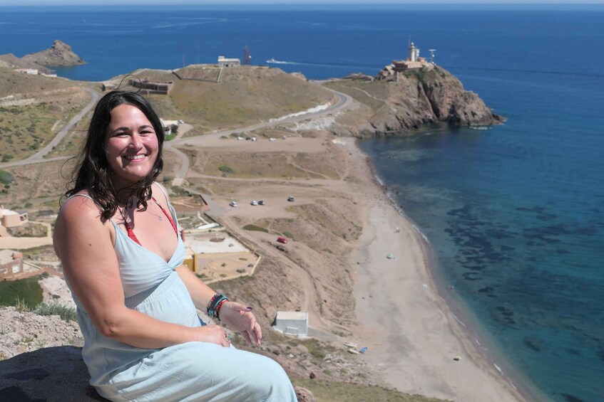 A person sitting on a cliff overlooking a coastal landscape with a lighthouse and a winding road. 3