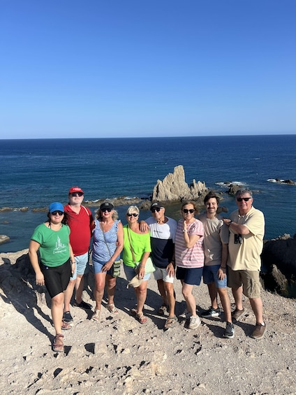 A group of people standing on a rocky shore with the ocean in the background. 1