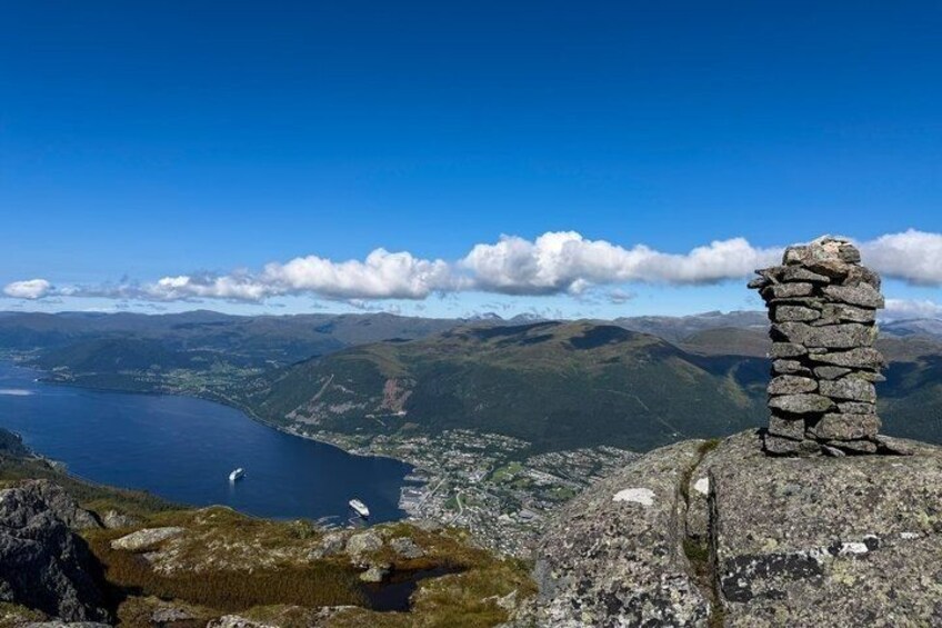 A stone cairn on a mountain peak overlooking a lake and distant mountains. 2