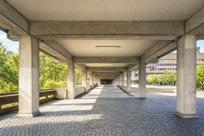 A covered pedestrian walkway with concrete pillars and cobblestone flooring. 3