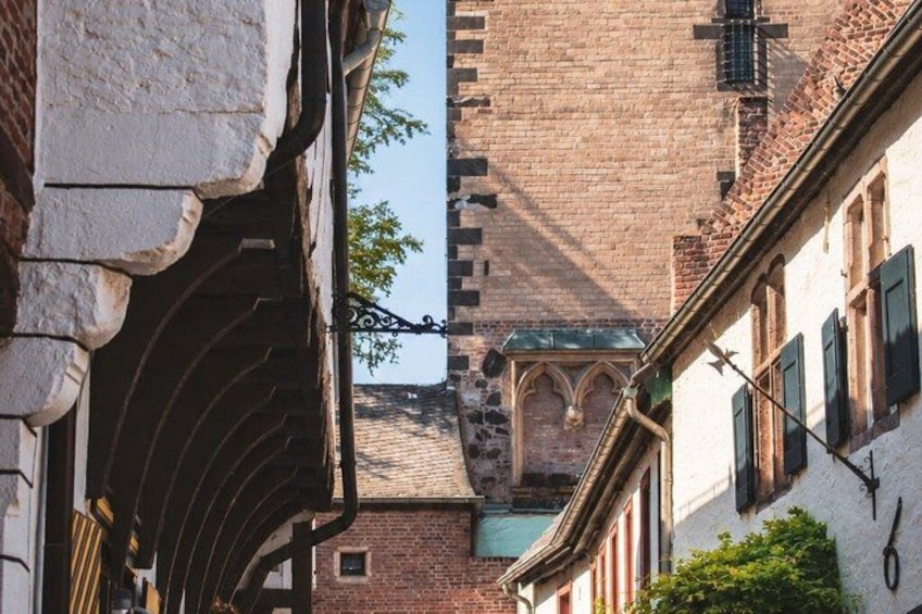 A narrow street with old buildings, a brick tower, and a wrought iron gate. 3