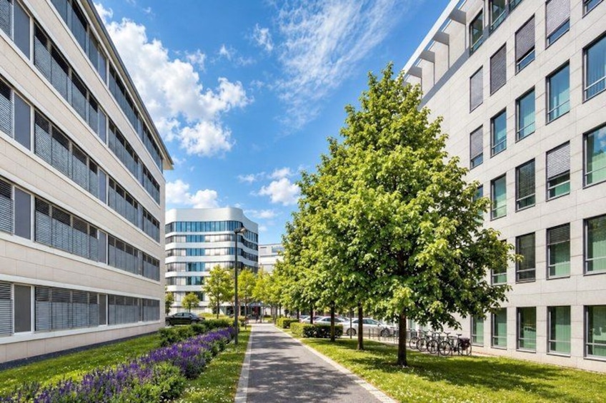 A modern urban street with buildings, a tree-lined sidewalk, and a clear sky. 2
