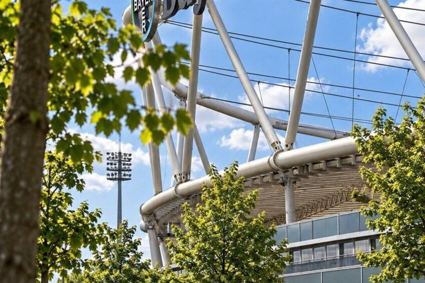Un estadio con una gran estructura de techo blanco y curvo, rodeado de árboles y un cielo despejado. 3