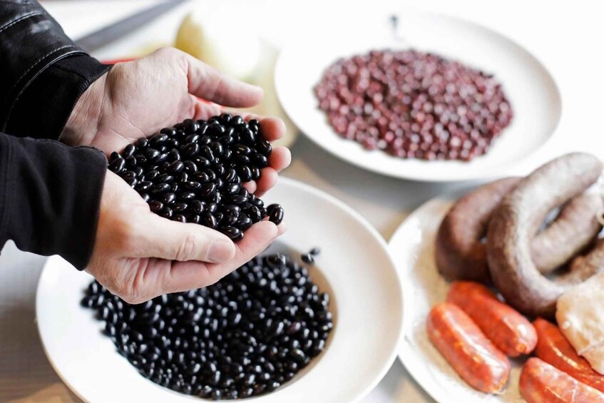 A person holding black beans, with plates of red beans and sausages in the background. 2
