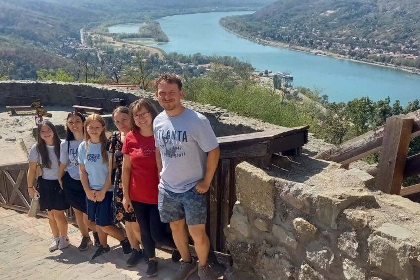 A group of people standing on a stone platform overlooking a river and a town. 3