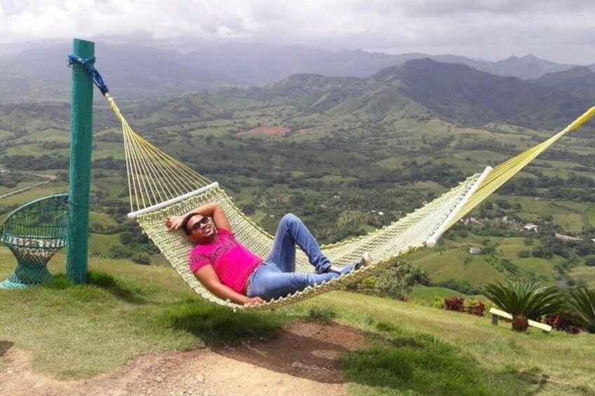 A person relaxing in a hammock on a grassy hill with a mountainous landscape in the background. 3
