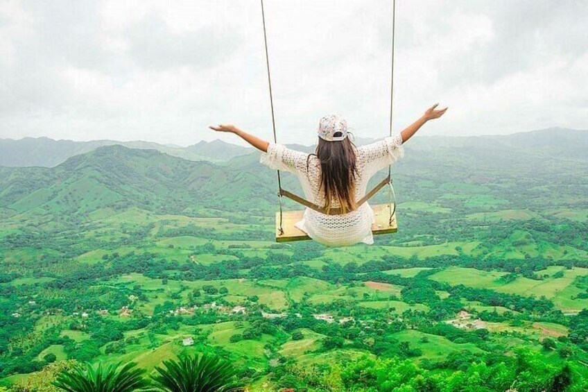 A person on a swing overlooking a green landscape with hills. 5