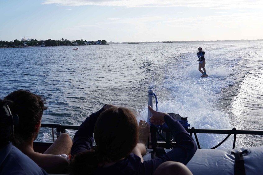 Eine Person betreibt Wakeboarden auf dem Wasser, während Zuschauer ein Boot beobachten. 5