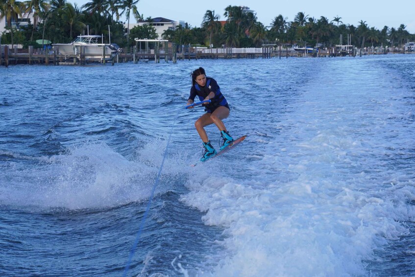 Eine Person beim Wakeboarden auf dem Wasser, im Hintergrund Palmen und Gebäude. 2