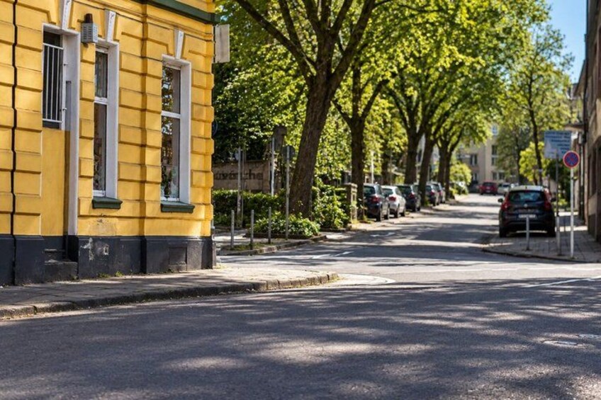 A yellow building with white trim, a tree-lined street, parked cars, and a no parking sign. 5