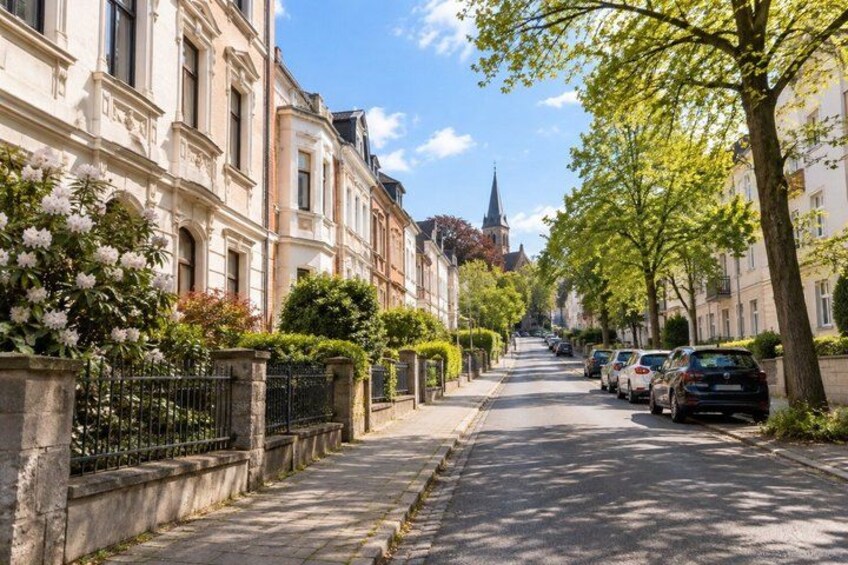 A tree-lined street with parked cars and historic buildings. 3