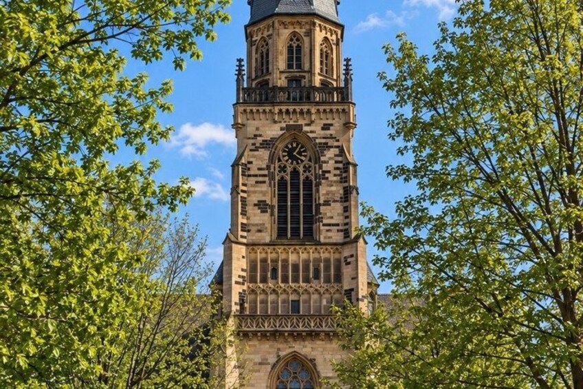 A tall, historic clock tower with intricate architectural details, surrounded by lush green trees. 2