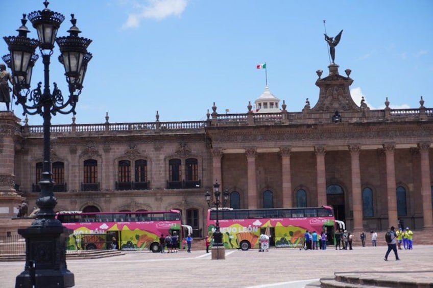 A historic building with a statue, a flag, and a colorful bus in the foreground. 5