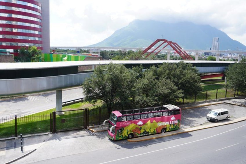 A colorful double-decker bus parked on a road with a bridge and mountains in the background. 3