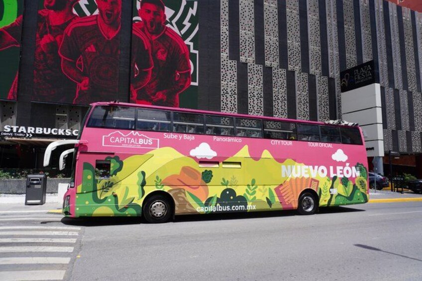 A double-decker bus with colorful graphics and text advertising a tour in Nuevo León, Mexico. 1