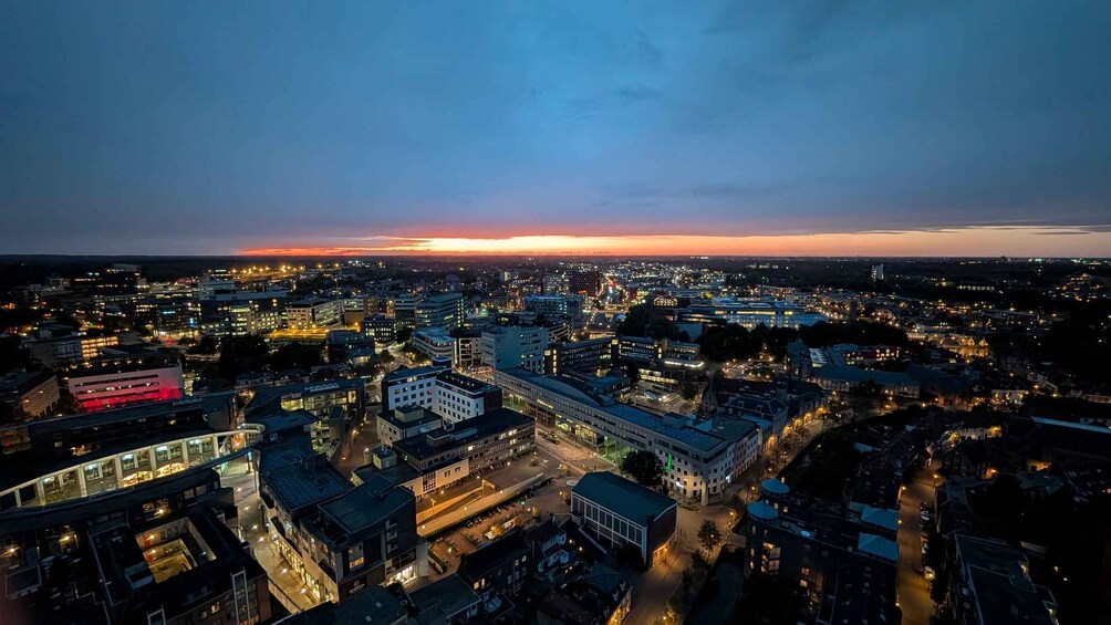 A cityscape at dusk with illuminated buildings and a sunset in the distance. 1