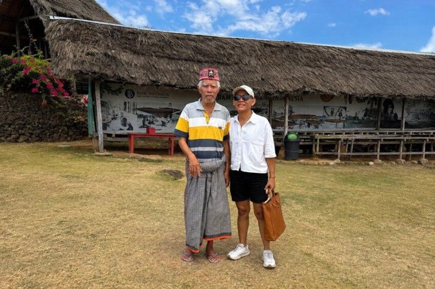 A man and a woman standing in front of a traditional thatched-roof building with a signboard. 5