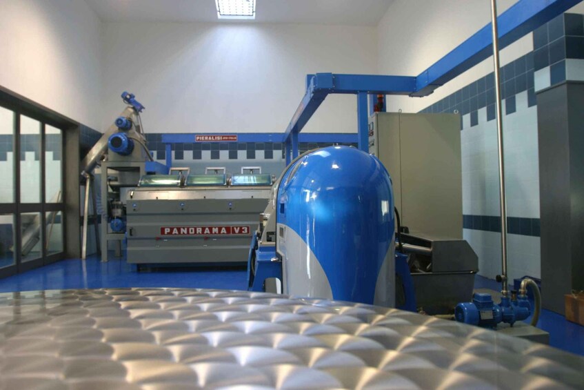 A large industrial machine labeled 'PANDRAMAV3' in a factory setting with blue and white walls, a blue floor, and a large blue tank in the foreground. 4