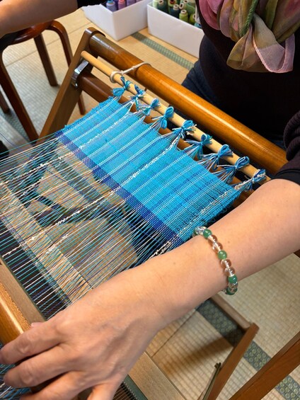 Iemand weeft op een houten weefgetouw met blauwe en witte draden. 2