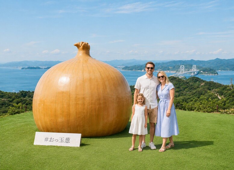A family standing in front of a large sculpture on a grassy field with a coastal landscape in the background. 2