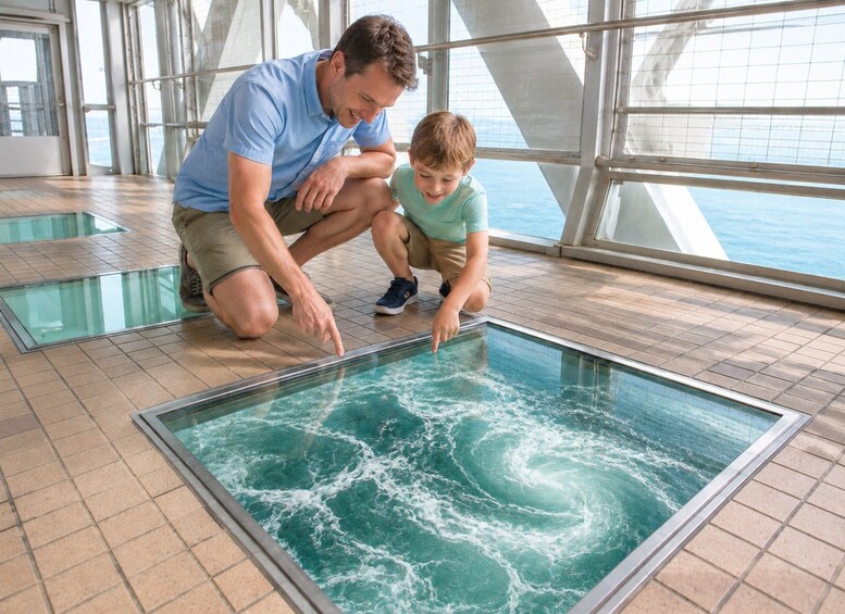 A man and a child observing a large indoor water feature with swirling water. 1