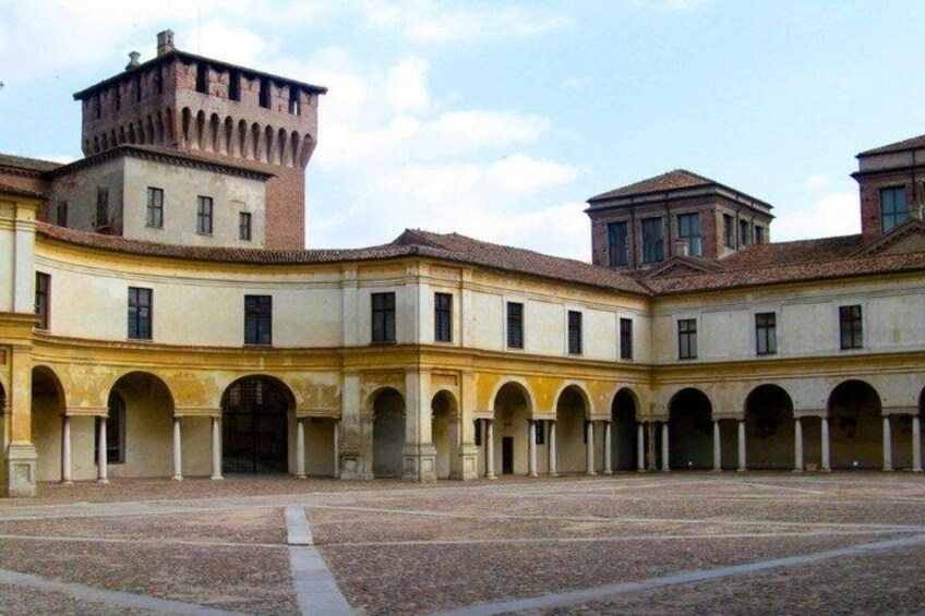 A courtyard with a central open space, surrounded by arches and buildings with a tower. 3