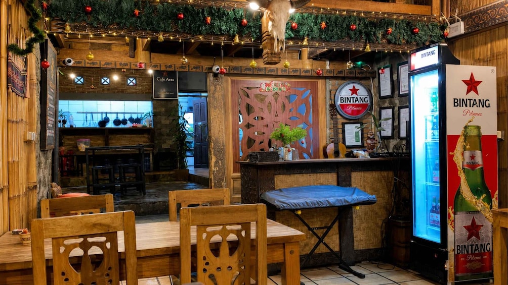A cozy cafe with wooden furniture, a Christmas sign, and a Bintang beer dispenser. 2