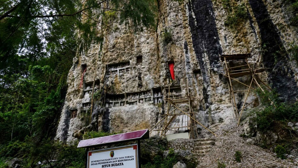 A rock face with carved figures and a sign indicating a historical site. 5