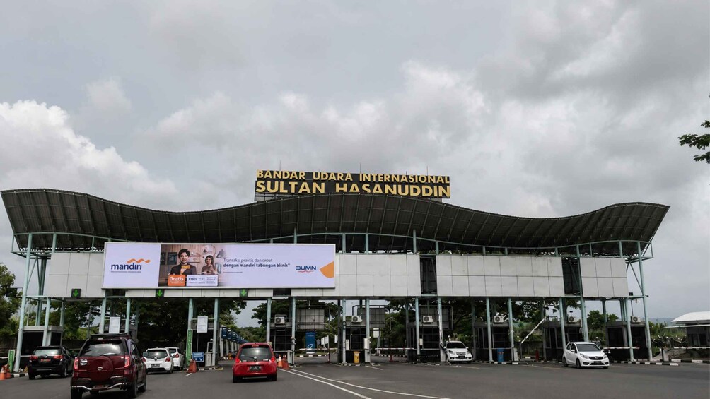 A toll booth with a large sign reading 'Bandar Udara Internasional Sultan Hasanuddin' and a billboard advertising a car service. 4