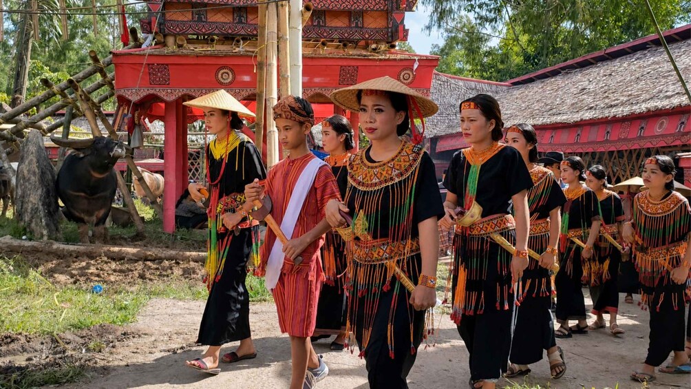 A group of people in traditional attire walking in front of a red temple with intricate designs. 3