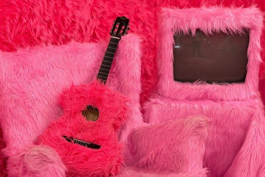 A pink furry chair with a guitar and a television screen. 5