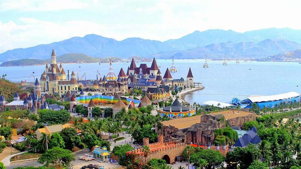 A coastal amusement park with a castle-like structure, a beach, and mountains in the background. 1