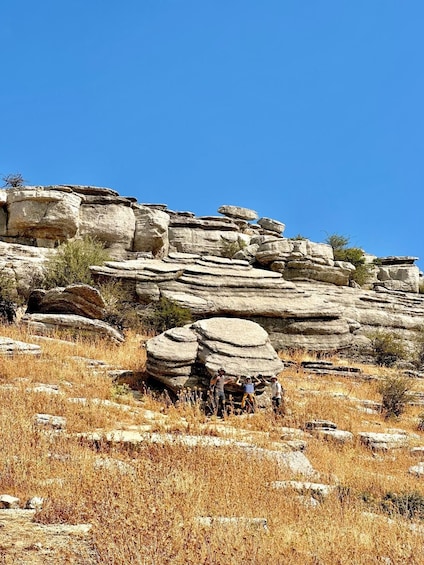 A rocky landscape with layered rock formations and dry grass. 2