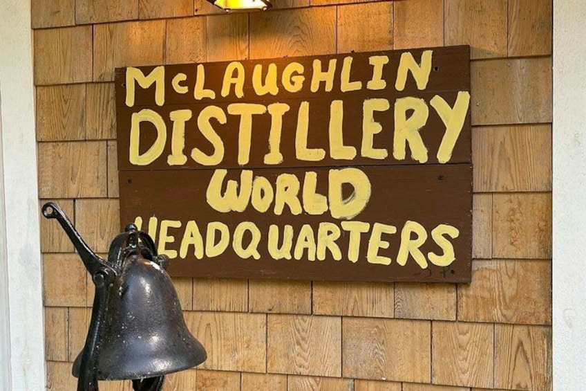 A wooden wall with a sign that reads 'McLaughlin Distillery World Headquarters.' 2