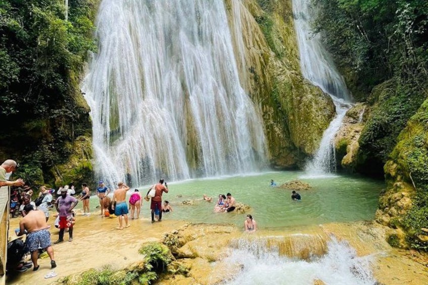 A waterfall, a pool of water, and people swimming and standing around. 3