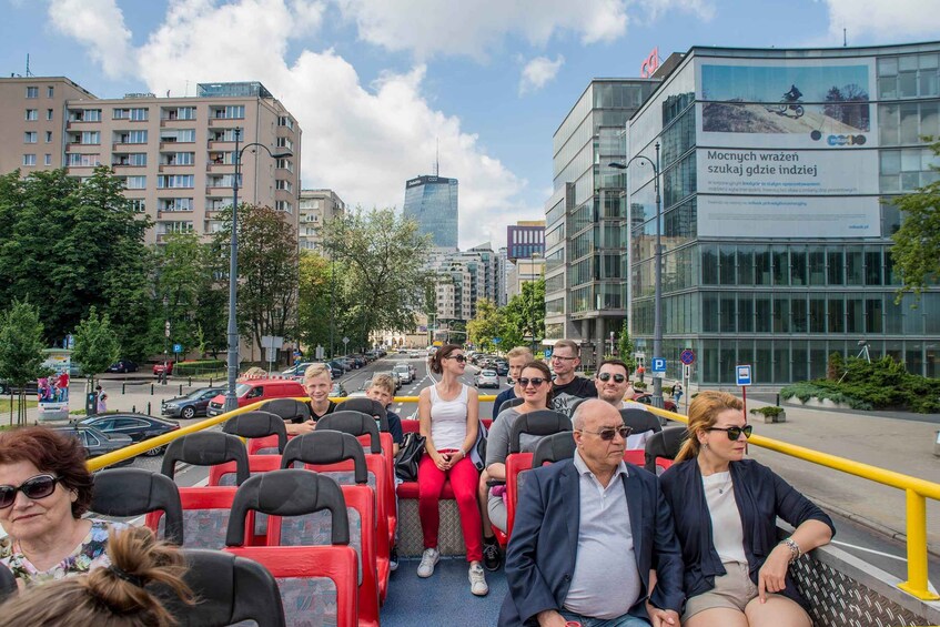 A group of people on a red bus, with modern buildings and a clear sky in the background. 4