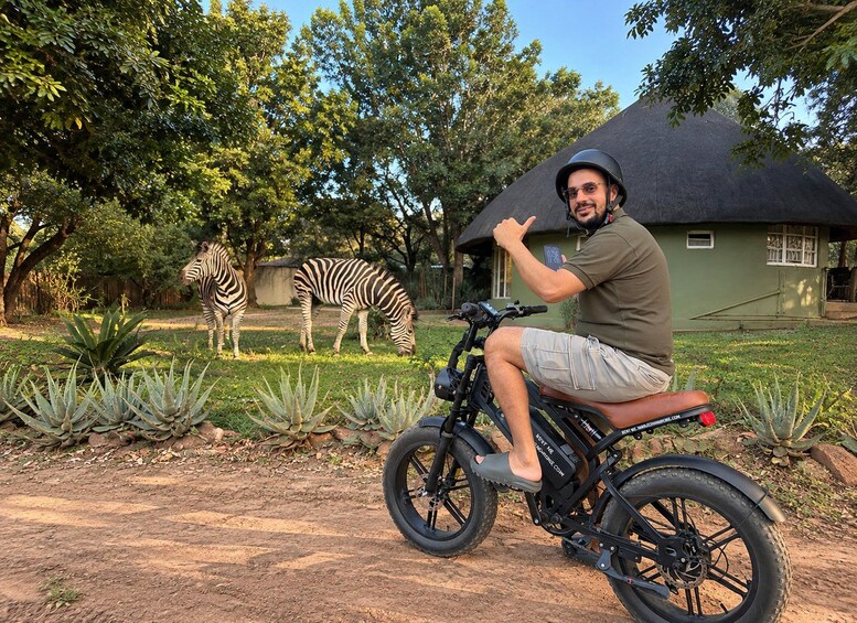 A person on a motorcycle in a natural setting with a zebra in the background. 2
