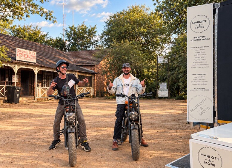 Two people on motorcycles in front of a signboard listing activities and vehicle rentals. 3