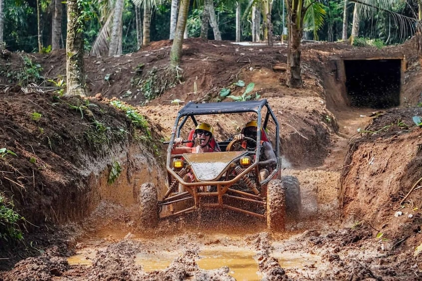A four-wheeled off-road vehicle navigating through a muddy terrain with a forested background. 2