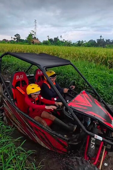 A red and black off-road vehicle with two passengers wearing helmets, driving through a field. 4