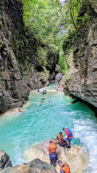 A group of people in a river surrounded by rocky cliffs and greenery. 3
