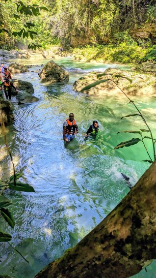 People wading in a clear river surrounded by rocks and greenery. 2