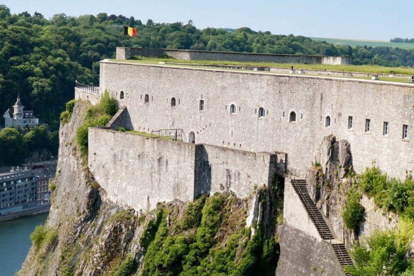 A historic stone fortress with a flag, steep cliffs, and a river. 5