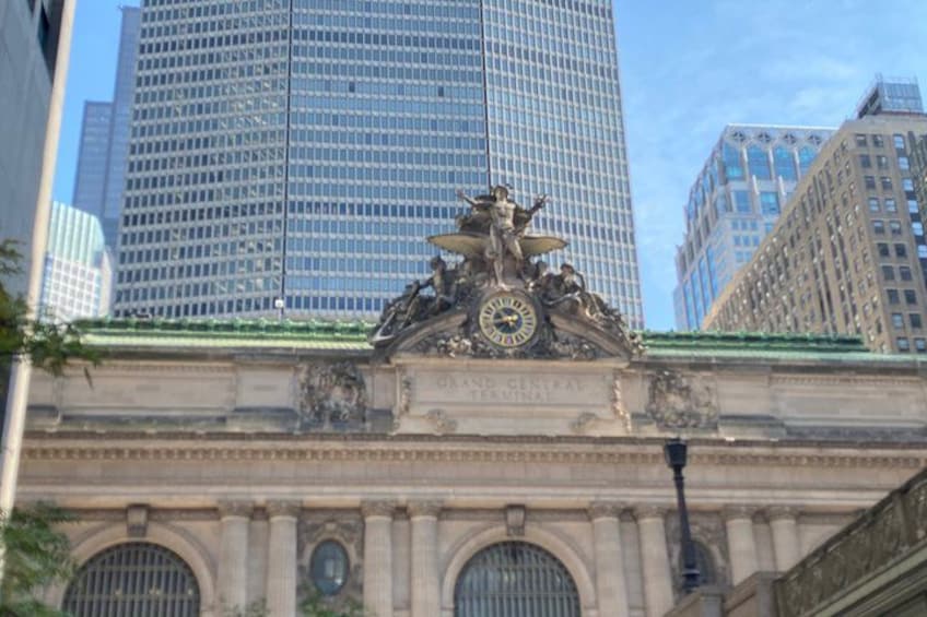 A classical building with a clock and ornate sculptures, surrounded by modern skyscrapers. 5